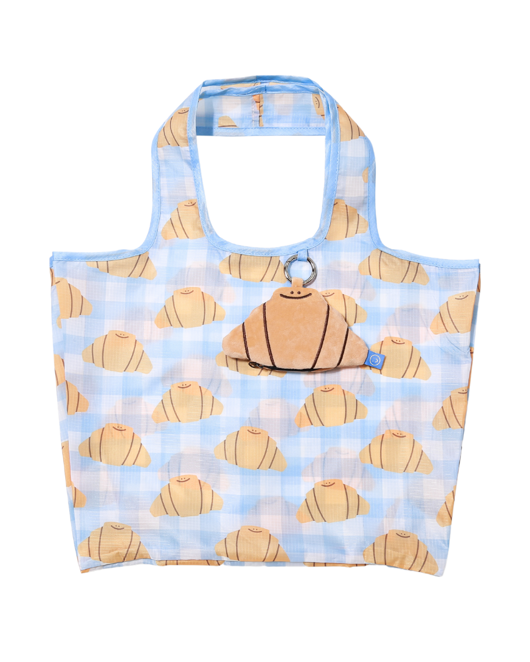 a croissant plushie hanging onto a large graphic printed reusable bag