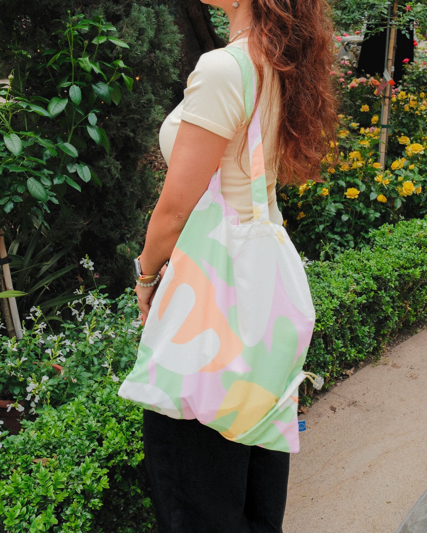 Person holding a colorful tote bag in a garden setting