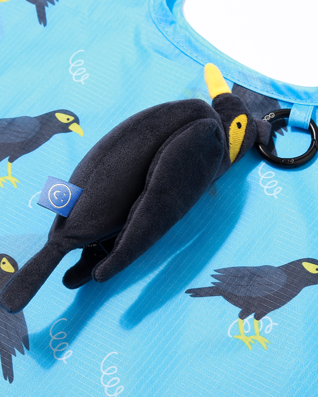 Black mynah bird plush exterior plushie bag charm hanging on a blue reusable bag