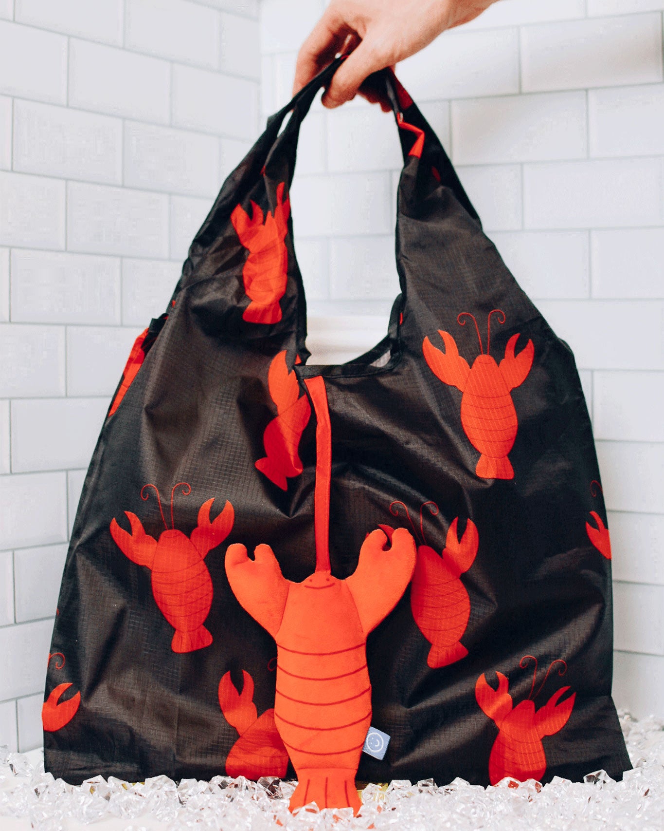 Lobster plushie hanging outside from a lobster printed reusable bag