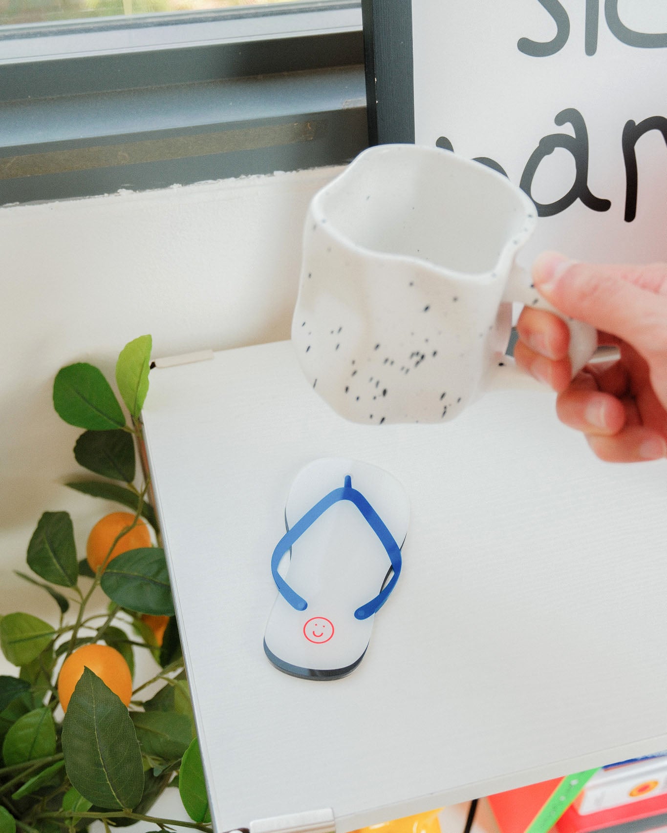 Person holding a white mug with black speckles over a white surface with a small blue and white device.